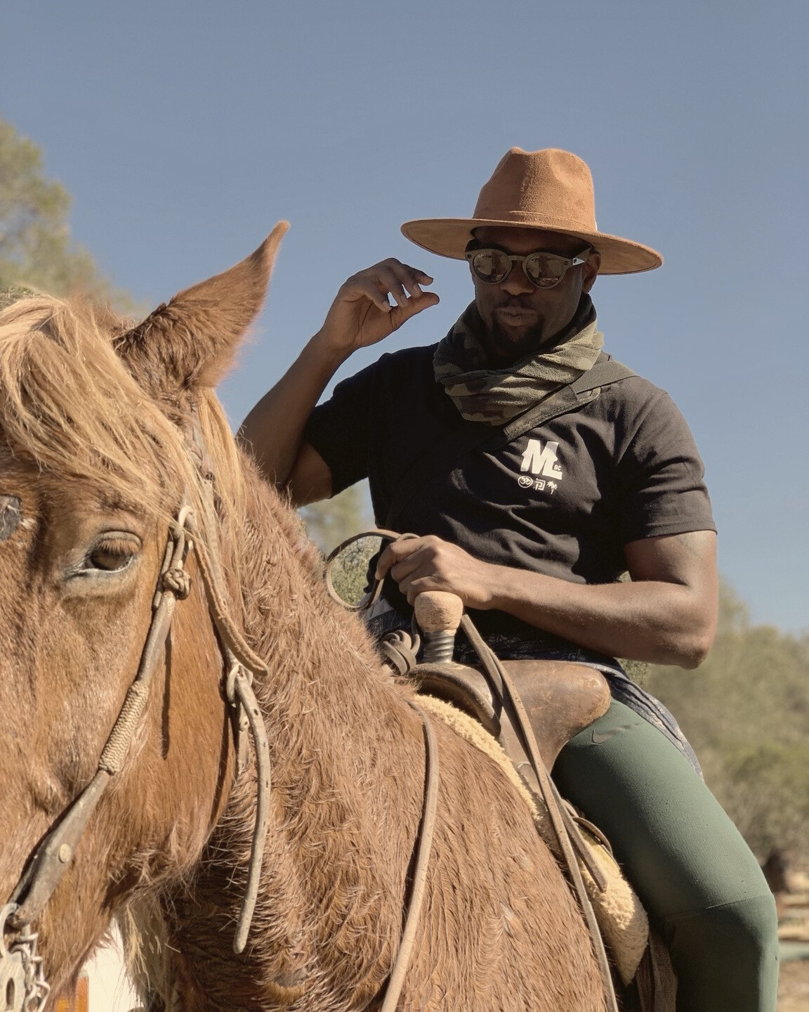 Un participante con sombrero café y lentes de sol monta un caballo alazán a plena luz del día.